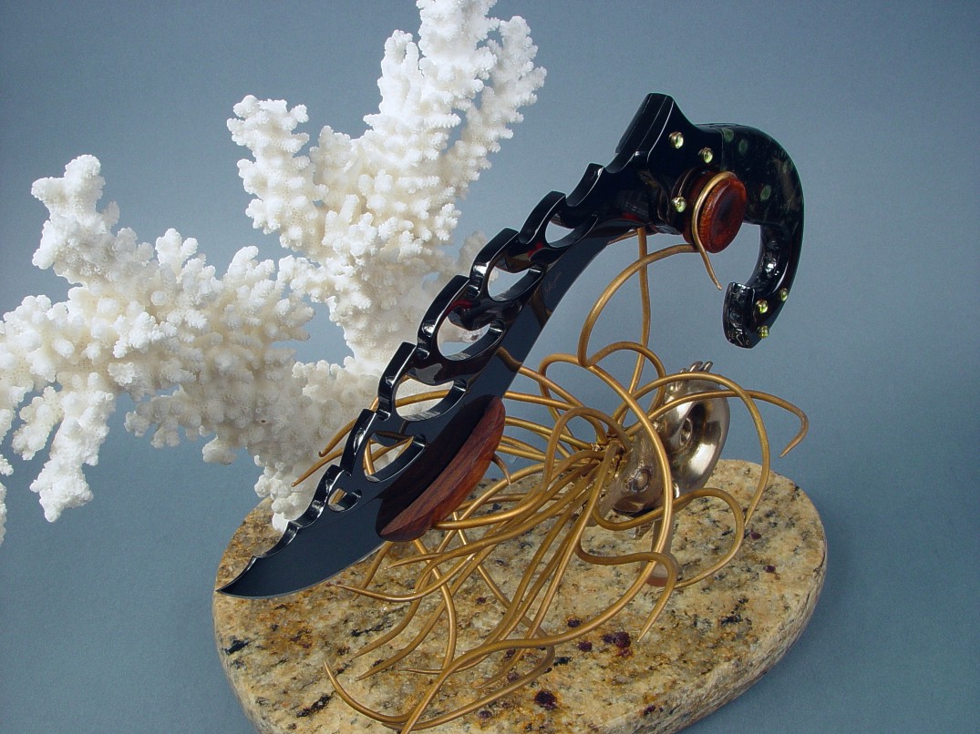 "Aegir" knife sculpture in mirror polished, hot blued O1 high carbon tungsten-vanadium alloy tool steel blade, blued steel bolsters, 14kt gold bezels, peridot gemstones, Nebula stone gemstone handle, stand of cast bronze, white Carribean coral, Venetian gold granite with garnets