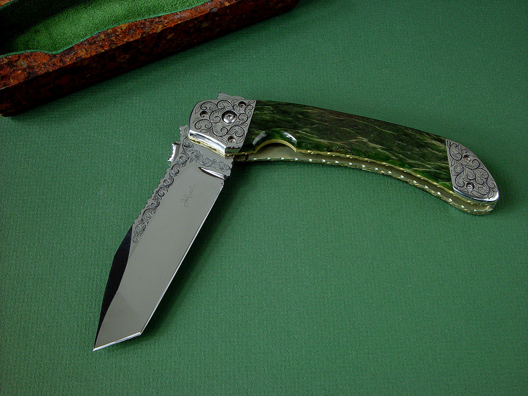 "Procyon" liner lock folding knife, obverse side view,in hand-engraved ATS-34 high molybdenum stainless steel blade, hand-engraved 304 stainless steel bolsters, anodized 6AL4V titanium liners and lockplate, Pounamu New Zealand Greenstone Nephrite Jade gemstone handle, case of Granite, Quartz Terrazzo composite