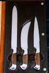 "Bordeaux, Courbe Vaste, Thresher" fine handmade chef's knives, BBQ knives, obverse side view in T3 cyrogenically treated 440C high chromium stainless steel blades, 304 stainless steel bolsters, Caprock petrified wood gemstone handles, Bison (American Buffalo), leather shoulder book case